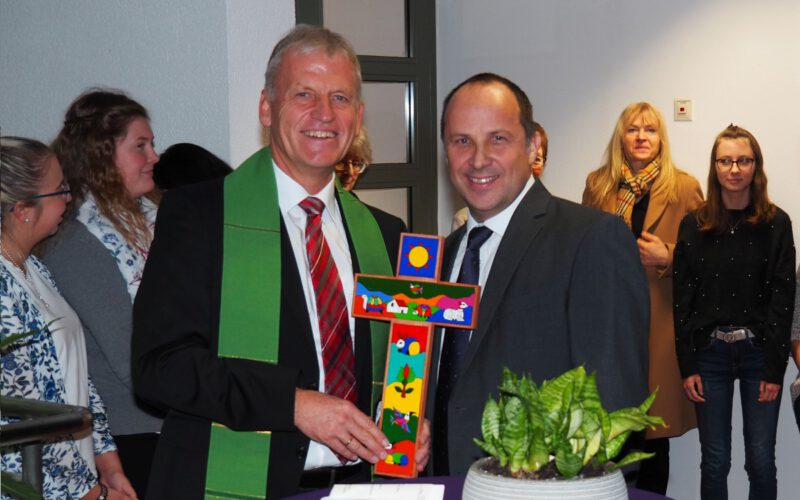 Dekan Peter Bertram (links) überreicht Vorstand Andreas Karau ein Kreuz für die neue Geschäftsstelle.
