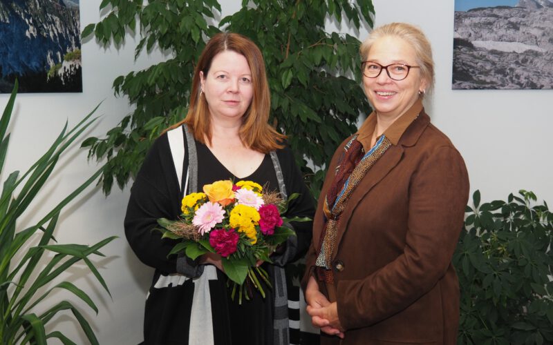 Dagmar Palwitz (rechts), Bereichsleiterin Finanzwesen, begrüßt Eva Perl an ihrem ersten Arbeitstag mit einem Blumenstrauß.