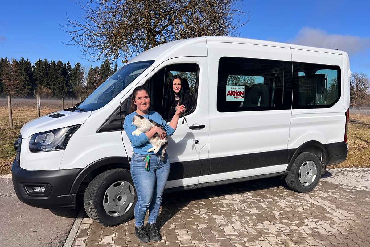 Einrichtungsleitung Caroline Bachmann (links) mit Hauskatze übergibt den Autoschlüssel des neuen Busses für die erste Fahrt an die pädagogische Fachkraft Nina Hocher.