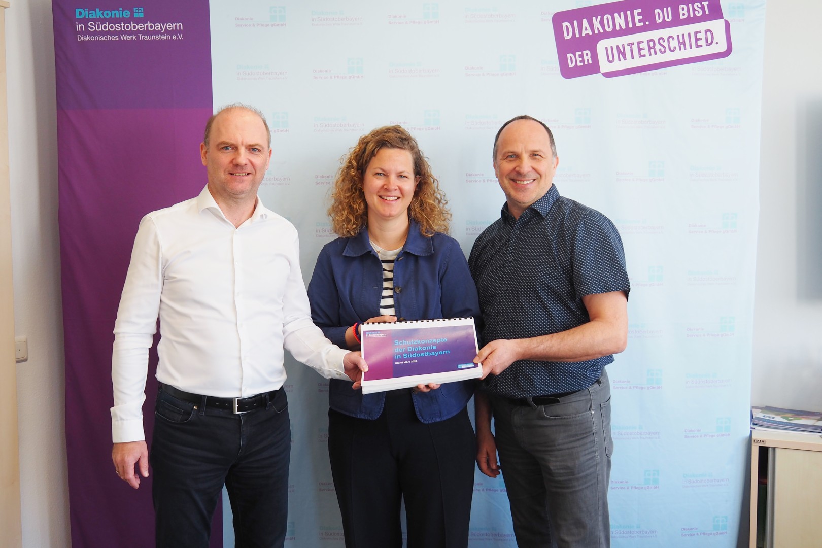 Julia Buchhorn, Präventionsbeauftragte der Geschäftsstelle, überreicht die gebündelten Schutzkonzepte an die Vorstände Andreas Karau (rechts) und Martin Schmid.