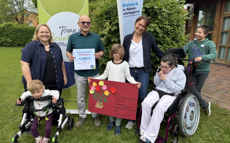 Große Freude bei der Spendenübergabe der Town & Country Stiftung an die Offene Behindertenarbeit Altötting: Kinder überreichen ein Plakat als Zeichen ihrer Freude über die Unterstützung für das Projekt „Andersgleich – Inklusion spielend erleben“. Stiftungsbotschafter Oliver Zahn übergibt die Spendenurkunde. (von links) Daniela Thalhammer (OBA Altötting), Oliver Zahn (Town & Country Stiftung) und Manuela Weiß (OBA Altötting).