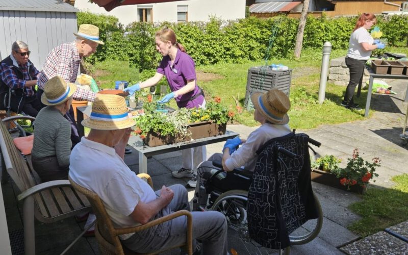 Bewohnerinnen und Bewohner bepflanzen gemeinsam mit Mitarbeitenden sommerliche Blumenkästen