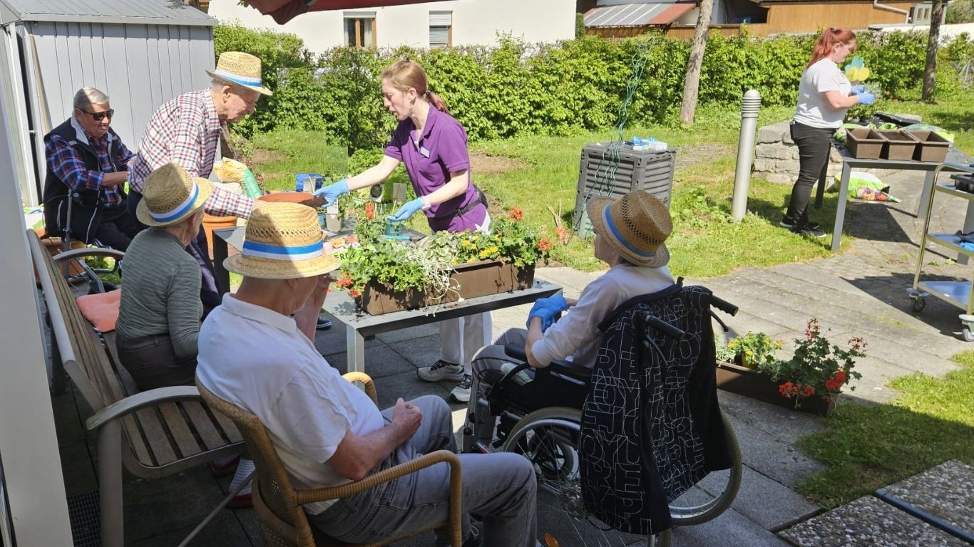 Bewohnerinnen und Bewohner bepflanzen gemeinsam mit Mitarbeitenden sommerliche Blumenkästen